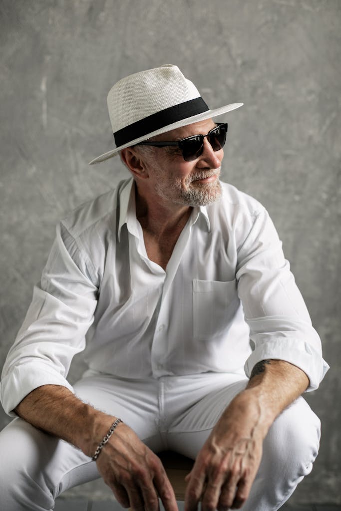 Elderly man wearing a fedora and sunglasses, posing confidently in a studio setting.